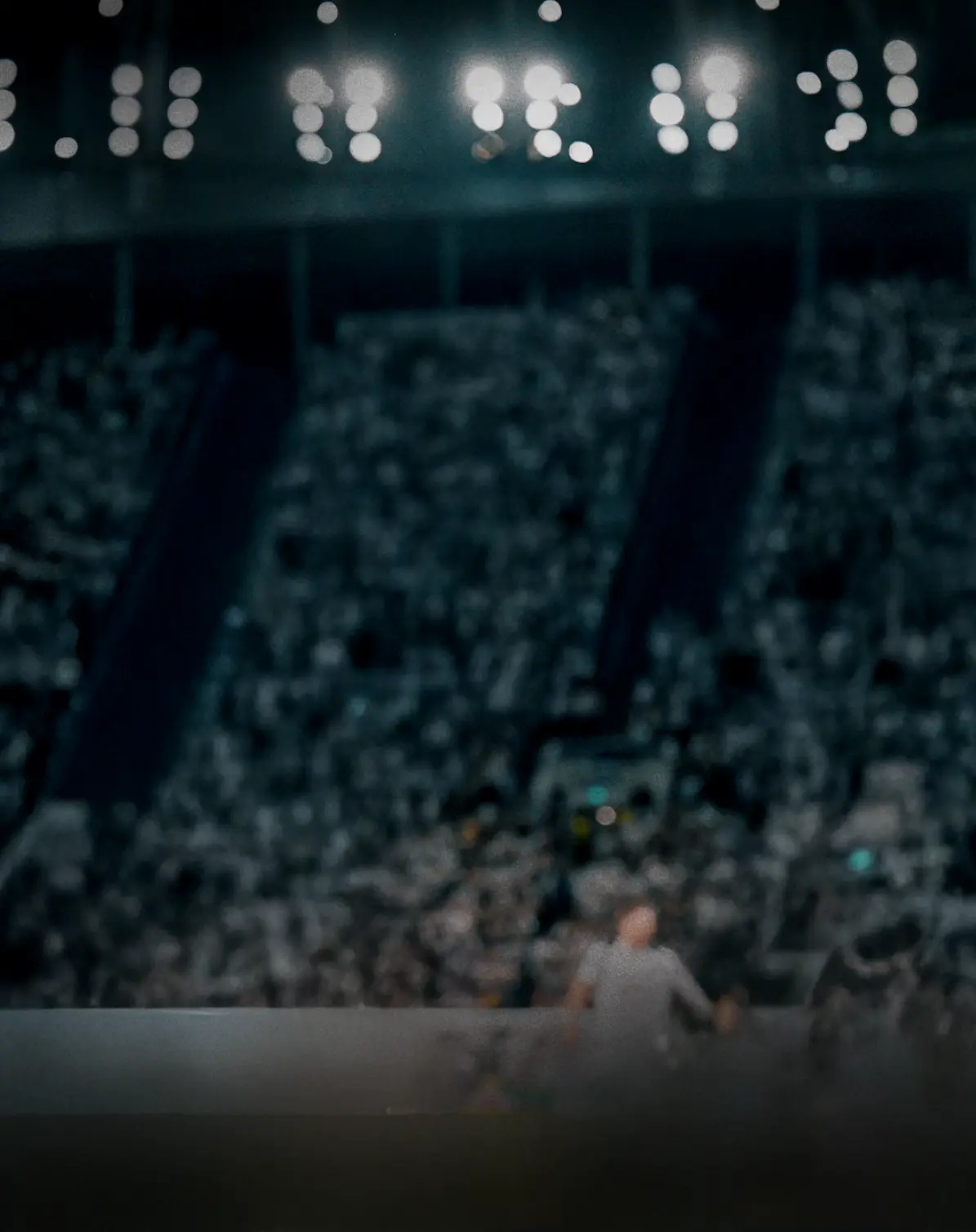 Vista sfocata di uno stadio di calcio affollato di notte, con fari luminosi e tribune gremite.